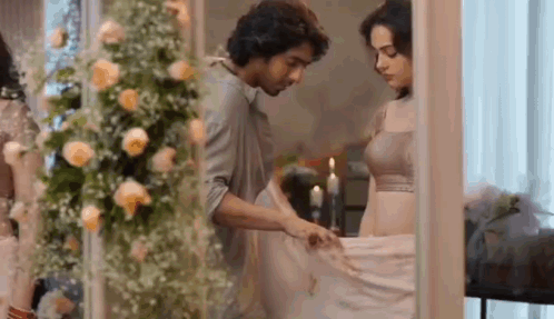 A Man And A Woman Are Standing Next To Each Other In A Room With Flowers And Candles . GIF