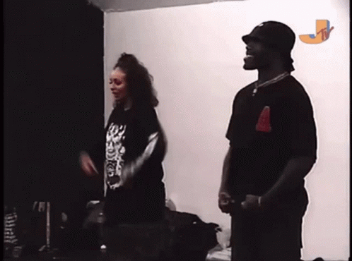 A Man And A Woman Are Standing Next To Each Other In A Room With The Letter J On The Wall GIF