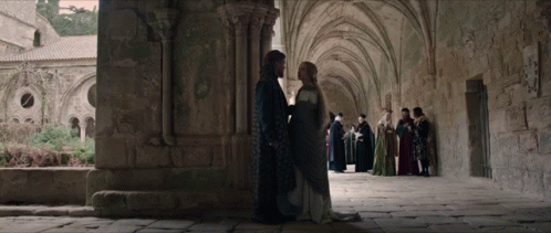 A Man And A Woman Are Standing Next To Each Other In A Stone Building GIF