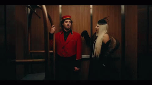 A Man And A Woman Are Standing Next To Each Other In An Elevator . GIF