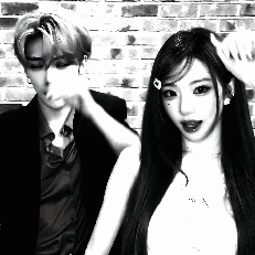 A Man And A Woman Are Standing Next To Each Other In Front Of A Brick Wall In A Black And White Photo . GIF