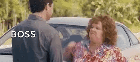 A Man And A Woman Are Standing Next To Each Other In Front Of A Car And The Woman Is Yelling At The Man . GIF
