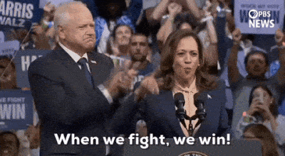 A Man And A Woman Are Standing Next To Each Other In Front Of A Crowd Of People . GIF
