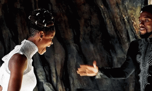A Man And A Woman Are Standing Next To Each Other In Front Of A Rock Wall . GIF