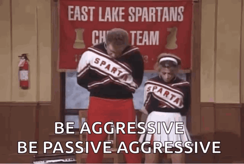 A Man And A Woman Are Standing Next To Each Other In Front Of A Sign That Says East Lake Spartans Cheer Team . GIF
