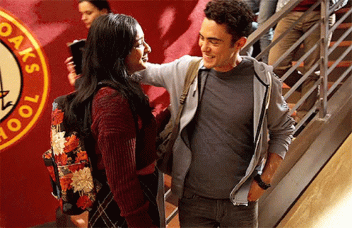 A Man And A Woman Are Standing Next To Each Other In Front Of A Sign That Says Oak 'S School GIF