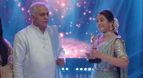 A Man And A Woman Are Standing Next To Each Other On A Stage . GIF