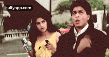 A Man And A Woman Are Standing Next To Each Other On A Street . The Man Is Pointing At The Woman . GIF