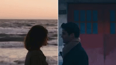 A Man And A Woman Are Standing Next To Each Other On The Beach And Looking At Each Other . GIF