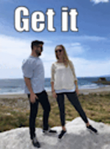 A Man And A Woman Are Standing Next To Each Other On Top Of A Hill Near The Ocean . GIF