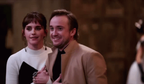 A Man And A Woman Are Standing Next To Each Other Smiling GIF