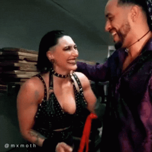 A Man And A Woman Are Standing Next To Each Other Smiling And Laughing . GIF