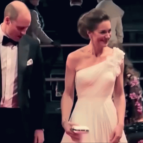 A Man And A Woman Are Standing Next To Each Other . The Woman Is Wearing A White One Shoulder Dress . GIF