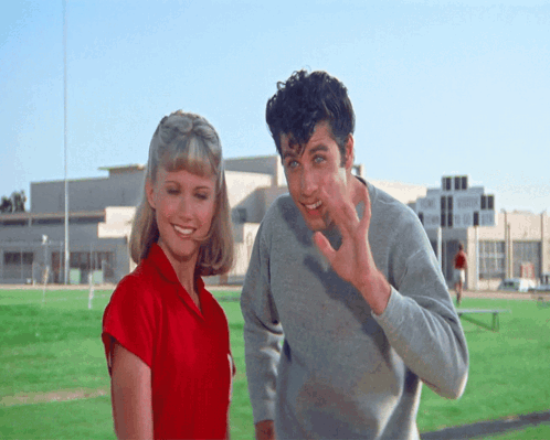 A Man And A Woman Are Standing On A Field And The Man Is Waving GIF