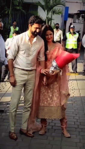 A Man And A Woman Are Standing On A Sidewalk Holding Hands GIF