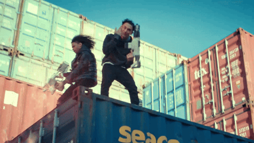 A Man And A Woman Are Standing On Top Of A Seaco Shipping Container GIF