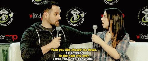 a man and a woman are talking in front of a sign that says emerald city comic con