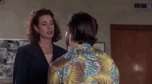 A Man And A Woman Are Talking To Each Other In A Room . The Man Is Wearing A Hawaiian Shirt . GIF