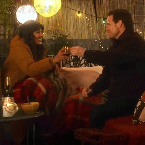 A Man And A Woman Are Toasting With Wine And The Words Love Again Are On The Bottom Right GIF