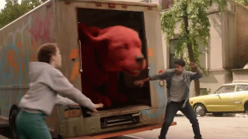 A Man And A Woman Are Trying To Get A Stuffed Red Dog Out Of The Back Of A Truck GIF