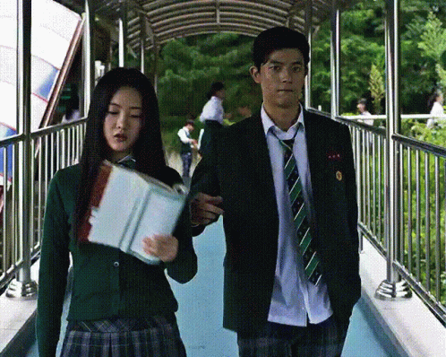 a man and a woman are walking across a bridge and the woman is holding a book