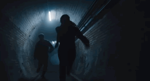 A Man And A Woman Are Walking Down A Dark Tunnel Holding Hands . GIF