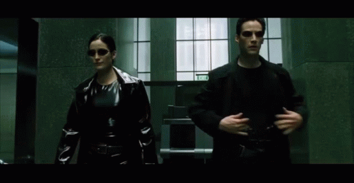 A Man And A Woman Are Walking Down A Hallway With A Sign That Says Exit On It GIF