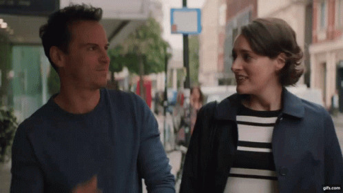 A Man And A Woman Are Walking Down A Street And Looking At Each Other . GIF