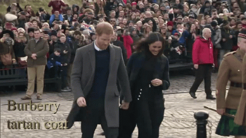 A Man And A Woman Are Walking In Front Of A Crowd Wearing A Burberry Tartan Coat GIF