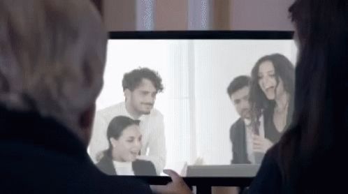 A Man And A Woman Are Watching A Group Of People On A Television Screen . GIF