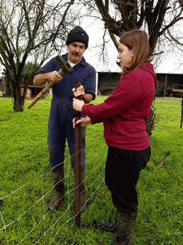 A Man And A Woman Are Working On A Fence Post GIF