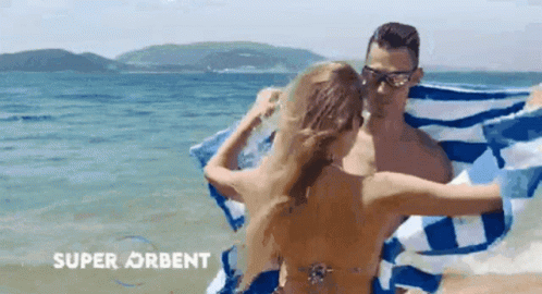 A Man And A Woman Are Wrapped In A Blue And White Striped Towel On A Beach .. GIF