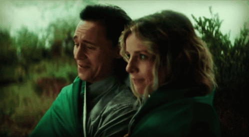 A Man And A Woman Are Wrapped In A Green Blanket And Looking At Each Other . GIF