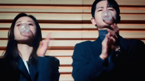 A Man And A Woman Blowing Bubbles In Front Of A Wall GIF