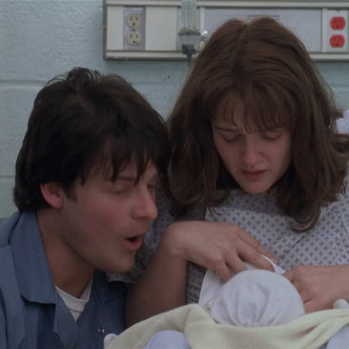 A Man And A Woman Holding A Baby In A Hospital Room GIF