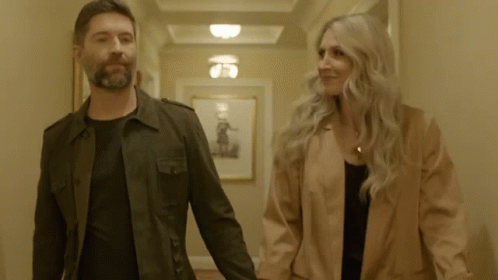 A Man And A Woman Holding Hands In A Hallway GIF