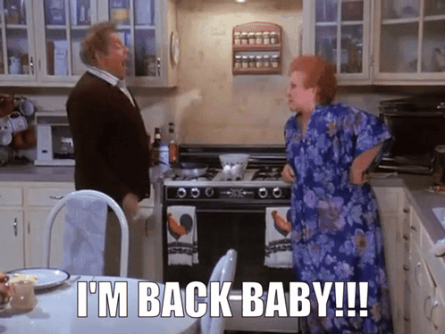 A Man And A Woman In A Kitchen With The Words " I 'M Back Baby " GIF