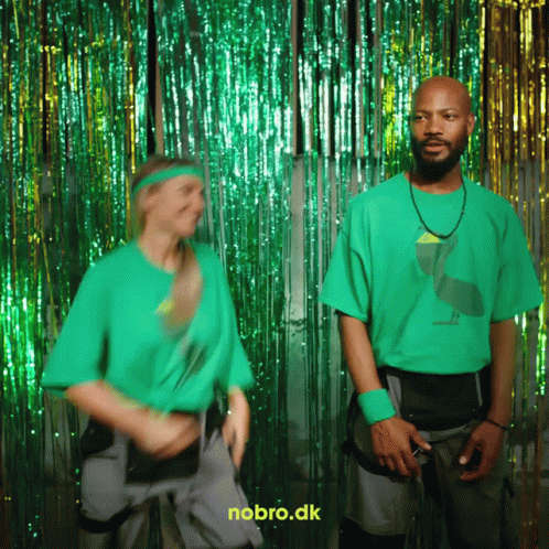 A Man And A Woman In Green Shirts Are Dancing In Front Of A Nobro.dk Sign GIF