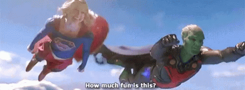 A Man And A Woman In Superhero Costumes Are Flying In The Air . GIF