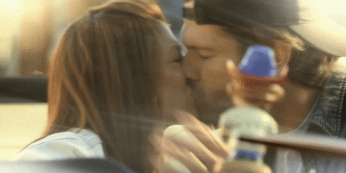 A Man And A Woman Kissing In A Car With A Bottle In The Background GIF