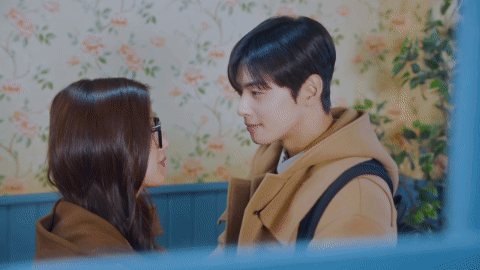 A Man And A Woman Kissing In Front Of A Floral Wall GIF