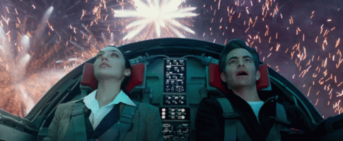 A Man And A Woman Looking Up At Fireworks In A Cockpit GIF