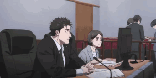 A Man And A Woman Sit At A Desk In Front Of A Computer GIF