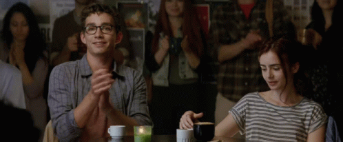 A Man And A Woman Sit At A Table Applauding In Front Of A Crowd GIF