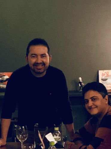 A Man And A Woman Sit At A Table In Front Of A Sign That Says B20 On It GIF