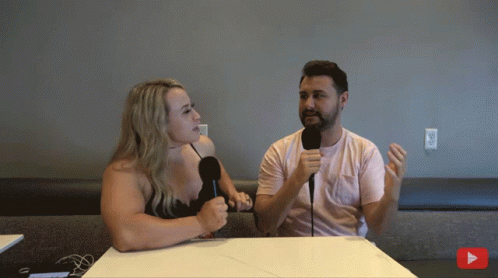 A Man And A Woman Sit At A Table With Microphones GIF