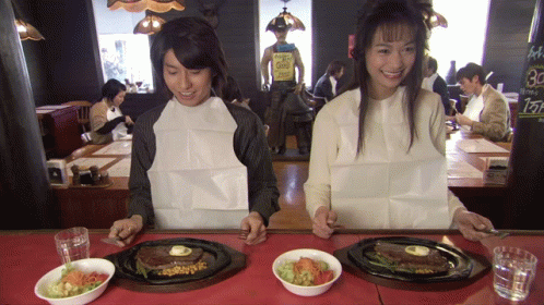 A Man And A Woman Sit At A Table With Plates Of Food And A Sign That Says 30 GIF