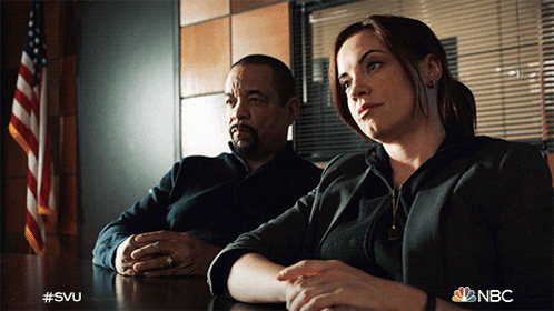 A Man And A Woman Sit At A Table With The Nbc Logo Visible GIF