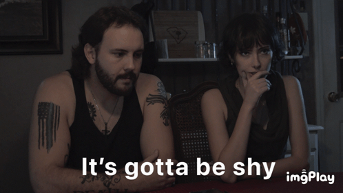A Man And A Woman Sit At A Table With The Words It 'S Gotta Be Shy GIF