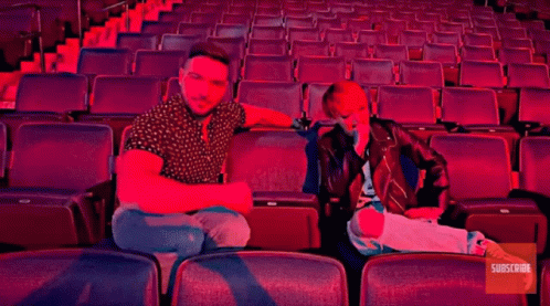 A Man And A Woman Sit In An Empty Auditorium With The Words Buc-Ee 'S GIF
